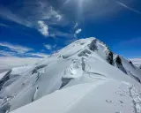 Śnieżna trasa na Mont Blanc, z widocznymi szczelinami lodowcowymi i śladami wspinaczy. Błękitne niebo z chmurami.