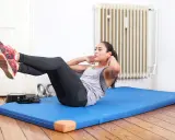 Frau macht Crunches auf einer blauen Matte. Sie trainiert ihren Bauchmuskel, um fit zu bleiben.