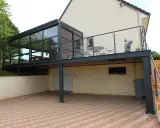 Modèle de véranda sur balcon avec structure métallique et vitrage. Un espace extérieur aménagé avec table et chaises.