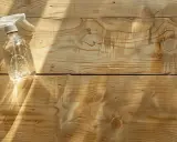 Bouteille de spray transparente avec un liquide et des bulles, posée sur des planches de bois clair. Idéal pour blanchir du bois.