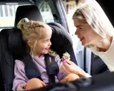 Uśmiechnięta mama daje córeczce w foteliku samochodowym bukiecik kwiatów. To miły test plus dla małej pasażerki.