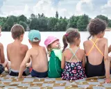 Dzieci siedzą na kocu nad jeziorem, ciesząc się fajnymi wczasami. Jedno z nich ma lody na twarzy.