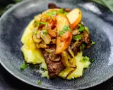 Gedünstete Leber mit Apfelspalten, Zwiebeln und Kartoffelpüree auf einem dunklen Teller.