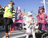 Japoński projektant mody inspiruje się stylem Harajuku. Cztery osoby w kolorowych, ekstrawaganckich strojach pozują na tle niebieskich schodów.
