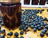 Ein Glas mit dunkler schlehen marmelade steht neben frischen Schlehen.