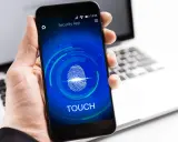 Dłoń trzyma smartfon z ekranem blokady "Security App" i ikoną odcisku palca. Proces autoryzacji jest w toku.