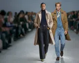 Para modeli na wybiegu w płaszczach i jeansach, z rozmytym tłem.