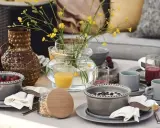 Vacker dukning runt bordet med frukostskålar, bär, juice och en vas med gula blommor.
