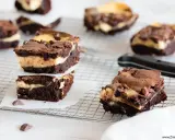 Schokoladige cheesecake brownies mit cremiger Füllung und Schokostückchen, gestapelt auf einem Gitter.
