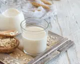 Szklanka i dzbanek z mlekiem owsianym, obok miseczka płatków owsianych. Idealne na zdrowe śniadanie, mleko 2 procent kcal.