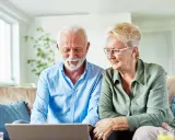 Uśmiechnięta para seniorów przegląda w internecie informacje, jak załatwiać sanatorium.