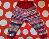 Pantalón de punto para bebé con rayas multicolores y cintura roja, sobre fondo de lunares.