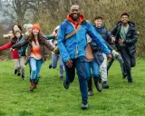 Lehrer und Schüler rennen lachend über eine grüne Wiese. Perfekt, um eine Klassenfahrt zu organisieren und Abenteuer zu erleben!