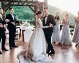 Para Młoda tańczy swój pierwszy taniec. Panna Młoda w pięknej sukni, Pan Młody w eleganckim garniturze. Druhny i świadkowie patrzą z uśmiechem.