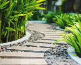 Un moderno camminamento giardino con lastre in pietra e ghiaia, circondato da rigogliosa vegetazione verde.