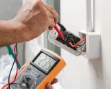 Elektryk sprawdza napięcie w gniazdku za pomocą multimetru, pokazując jak liczyć punkt elektryczny.