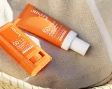 Deux produits solaires, un stick et un fluide, sont posés sur une serviette rayée. Le bouton du stick est visible, prêt à protéger du soleil.