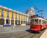 Röd spårvagn i Lissabon, perfekt för en resa med interrail europa. Gula byggnader och en triumfbåge i bakgrunden.