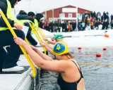 Deltagare gör sig redo för vintersim i Skellefteå. De håller i gula räcken och kliver ner i det kalla vattnet, med publik som tittar på.
