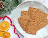 Assiette de sablés rennes de Noël, décorée de branches de sapin givrées, de ruban rouge et de tranches d'orange séchée.