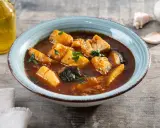 Un tazón de patatas con bacalao en salsa, decorado con perejil. Al lado, una botella de aceite de oliva y ajos.