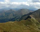 Widok na pasmo górskie, gdzie w Tatry prowadzi wydeptana ścieżka. Chmury na niebie.