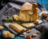 Kawałek parmezanu z nożem, okruchy sera, orzechy i bazylia. Czy parmezan można mrozić? Tak, można go mrozić, choć może stracić nieco na konsystencji.