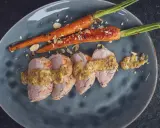 Zarte Scheiben von **schweinefilet grillen** mit Honig-Senf-Sauce und karamellisierten Karotten, bestreut mit Mandelsplittern.