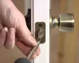 Mano usando un destornillador para desmontar una cerradura de puerta interior, quitando los tornillos de la placa.