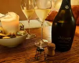 Zwei Gläser Champagner, eine Kerze und eine Flasche "Memory" auf einem Holztisch. Der Champagnergehalt ist hierbei nicht ersichtlich, aber die Stimmung ist festlich.