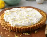 A lemon tart topped with whipped cream and lemon zest on a wooden board.