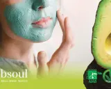 Donna con maschera viso fai da te verde, accanto ad avocado. Certificazioni bio e vegan.