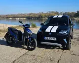 Niebieski skuter i czarne aixam auto z białymi pasami stoją nad rzeką.