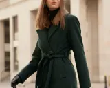 Elegancka kobieta w ciemnozielonym płaszczu z paskiem. Dowiedz się, jak prać płaszcz z wełny i poliestru, by służył latami.