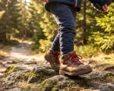 Jesienne wędrówki w lesie. Dziecko w brązowych, sznurowanych butach przemierza kamienistą ścieżkę. Idealne buty w góry jesienią to podstawa.