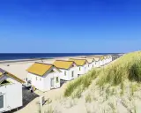 Reihen von weißen Strandhäusern mit gelben Dächern am **Holland Strand** unter blauem Himmel.