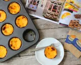 Pyszne, lekko przypieczone pastel de nata w blaszce i na talerzyku. Obok magazyn z widokiem na Lizbonę i tramwaje.