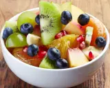 Kolorowa sałatka owocowa zimowa: kiwi, pomarańcza, winogrona, borówki, granat i brzoskwinia w białej misce.