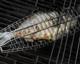 Ein ganzer Fisch wird in einem Grillkorb gegrillt. Die Haut ist goldbraun und leicht gebräunt.
