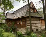 Drewniana chata z kamiennym fundamentem, kryta gontem, otoczona zielenią. Ulica Kościeliska w Zakopanem zachwyca tradycyjną architekturą.
