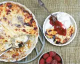 En gyllene falsk ostkaka med krispiga kanter, serverad med vispad grädde, sylt och färska hallon.