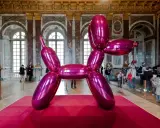 Jeff Coons' glänzender Ballonhund in Pink, ausgestellt in einem prunkvollen Saal mit Besuchern.