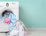 Lavadora blanca con ropa de colores y botella de detergente. Aprende como limpiar la lavadora para un mejor lavado.