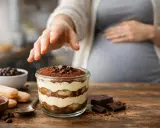 Une main effleure un tiramisu, un délice pour une femme enceinte. Le dessert, garni de cacao et de chocolat, promet un moment gourmand.