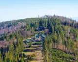 Widok na górskie schronisko na Babiej Górze, otoczone lasem iglastym i liściastym.