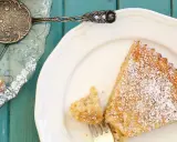 Saftige spanische Mandeltorte, bestäubt mit Puderzucker, auf einem weißen Teller. Ein Stück wurde bereits mit einer Gabel entnommen.
