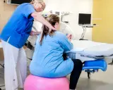 Barnmorska ger stöd åt en kvinna som sitter på en träningsboll, redo för förlossning under tredje trimestern.