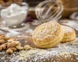 Deux biscuits pour entremet, saupoudrés de sucre glace, reposent sur un lit d'amandes concassées et entières.