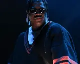 Lil Yachty w okularach i długich kolczykach, w swetrze z pomarańczowymi pasami. Let's start here.