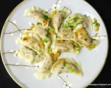 Pyszne pierogi z kaszą gryczaną, okraszone skwarkami i posypane natką pietruszki, na talerzu z delikatnym wzorem kwiatowym.